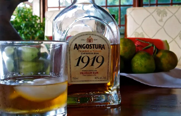 A glass of Angostura rum on the rocks with the bottle behind it